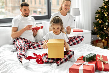 family, winter holidays and people concept - happy mother, father and little daughter opening christmas gifts in bed at home
