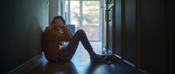 Sad Middle Aged Man Sitting on the Floor In the Hallway of His Appartment, Covering Face with...
