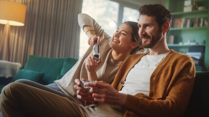 Happy Couple Sitting on the Sofa Playing Video Games, Using Controllers. Competitive Girlfriend and Boyfriend in Love have Fun Playing in Online Video Games at Home Together