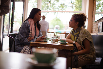 Young women friends talking and drinking cappuccinos at cafe table