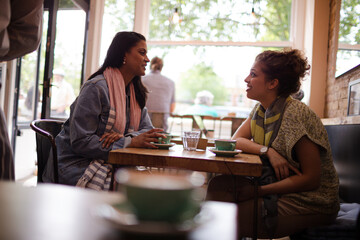 Young women friends talking and drinking cappuccinos at cafe table
