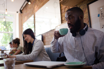 Young man with headphones drinking coffee in cafe