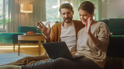 Lovely Couple Use Laptop Computer with Conference Video Call App to Chat, Wave Hello and Greet Friends, Relatives and Coworkers. Remote Work, Home Office, Staying in Touch with Friends and Family. © Gorodenkoff
