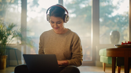 Young Woman Using Laptop at Home, Does Remote Work, Listens Music through Headphones. Beautiful...