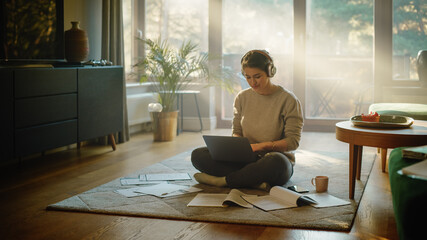 Young Woman Using Laptop at Home, Does Remote Work, Listens Music through Headphones. Beautiful...