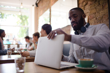 Man with headphones using laptop and drinking coffee in cafe