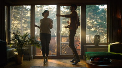 Happy Young Couple Dances in the Living Room. Cheerful Girlfriend and Boyfriend Enjoy True Love, Good Mood and Energetic Music Have Fun at Home. Stylish Interior and Sunny Day - obrazy, fototapety, plakaty