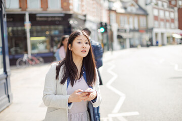 Young businesswoman with cell phone hailing taxi on sunny urban street