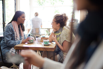Young women friends talking and drinking cappuccinos at cafe table