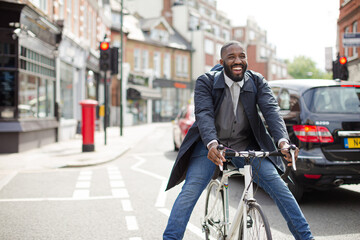 Playful young businessman commuting, riding bicycle on urban street