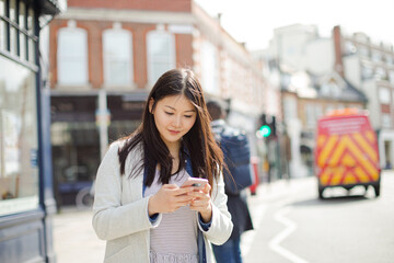 Young businesswoman with cell phone hailing taxi on sunny urban street
