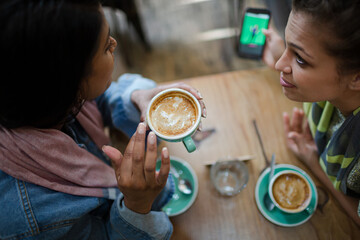 Female friends drinking coffee and using cell phone in cafe