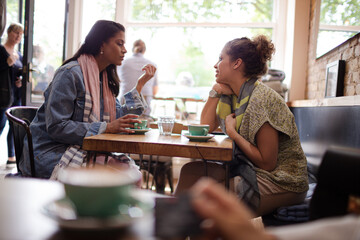 Young women friends talking and drinking cappuccinos at cafe table