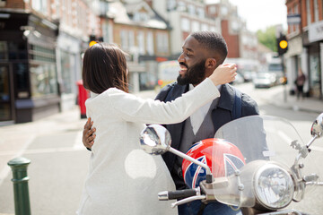Affectionate young couple hugging at motor scooter on sunny urban street