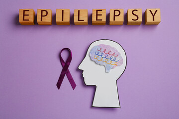 Human head cutout with brain, purple ribbon near word Epilepsy made of wooden cubes on lilac...