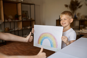 Little boy shows his drawing, kid in workshop
