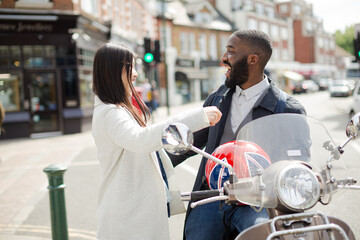Affectionate young couple hugging at motor scooter on sunny urban street
