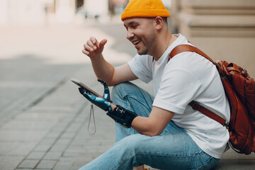 Young disabled man using mobile phone with artificial prosthetic hand in casual clothes outdoors - obrazy, fototapety, plakaty