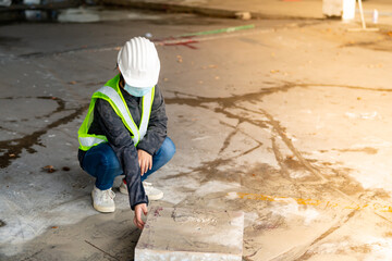 Young Asian female construction engineer   wearing a medical mask to cover her mouth and wearing a white safety helmet concrete plinth inspection cut from the floor, in the construction zone, camera