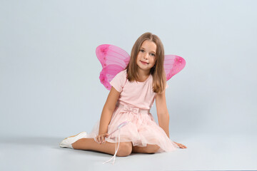 Cute little girl in fairy costume with pink wings and magic wand on light background