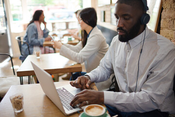Man with headphones using laptop and drinking coffee in cafe