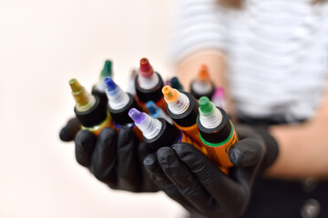 Woman master of tattooing holding bottles of colorful tattoo ink.