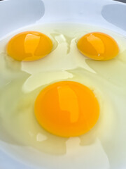 Three bright yellow raw chicken eggs in a white bowl.