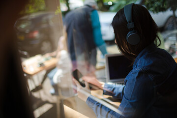 Young woman listening to music with headphones, texting with cell phone at cafe window