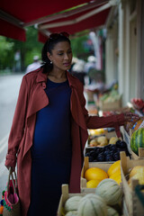 Pregnant woman shopping for produce at market storefront