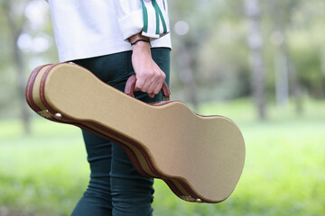 Woman holds violin and guitar case and walks through park