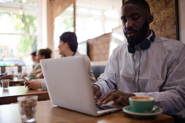 Man with headphones using laptop and drinking coffee in cafe