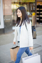 Smiling young woman walking along storefront with shopping bags