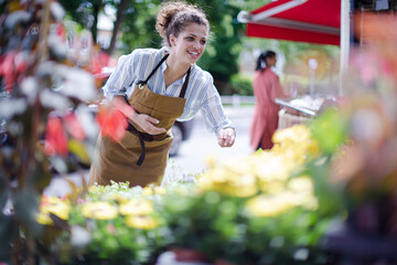 Female florist checking plants at sunny flower shop storefront