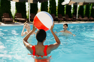 Smiling friends play with ball in the pool