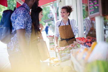 Female worker helping young couple shopping for fruit at market storefront