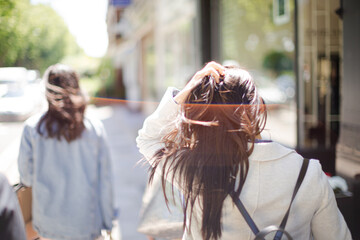 Young woman walking down urban street and playing with her hair