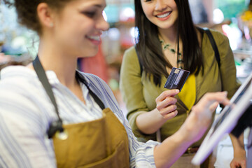 Smiling female shopper with credit card paying cashier at grocery store cash register