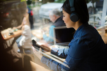 Young woman listening to music with headphones, texting with cell phone at cafe window