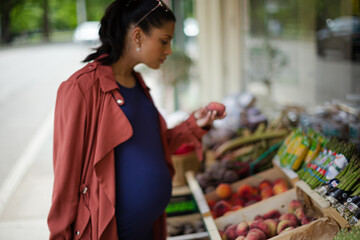 Pregnant woman shopping, smelling fruit at market storefront