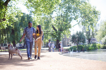 Obraz premium Happy young couple walking dog in sunny park