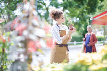 Naklejka premium Female florist checking plants at sunny flower shop storefront