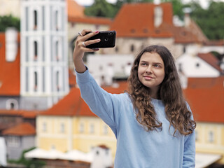Young girl takes a selfie photo on the background of the historic town, city Czech Krumlov, Czech republic