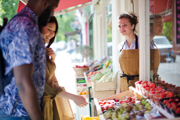 Female worker helping young couple shopping for fruit at market storefront