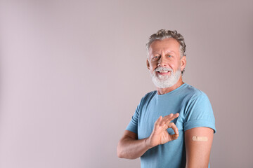Cheerful senior man showing arm with bandage after vaccination on beige background. Space for text