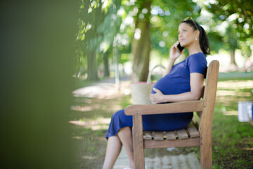Pregnant woman talking on cell phone on park bench