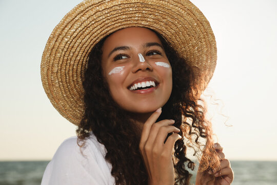Happy African American woman with sun protection cream on face near sea