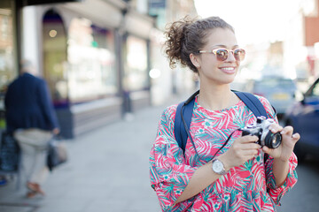 Portrait laughing, enthusiastic young female tourist in sunglasses photographing with camera on urban street