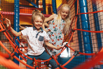 Happy group of siblings playing together on indoor playground. Excited kids playing together on net...