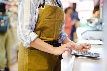 Female cashier using calculator in grocery store