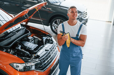 Professional service. Man in uniform is repairing broken automobile indoors